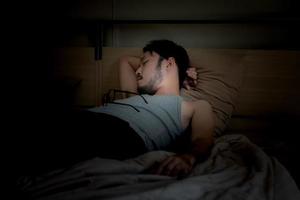 bello giovane uomo addormentato accogliente su un' letto nel il suo Camera da letto a notte. foto