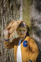 carino ragazzo in posa nel un' cowboy cappello nel il boschi di un' albero. il di sole raggi avvolgere il spazio. interazione storia per il libro. spazio per copiatura foto