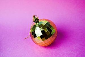 d'oro giallo piccolo il giro bicchiere plastica inverno inteligente brillante decorativo bellissimo natale festivo Natale sfera, Natale giocattolo incollato al di sopra di con lustrini su un' viola rosa sfondo foto