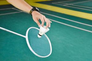 badminton giocatore detiene racchetta e bianca crema volano nel davanti di il netto prima servendo esso per un altro lato di il Tribunale. foto