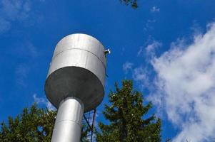 grande ferro metallo brillante inossidabile industriale acqua Torre per fornitura acqua con un' grande capacità, barile contro il blu cielo e alberi foto