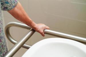 donna anziana asiatica paziente uso supporto WC in bagno, barra di sostegno di sicurezza corrimano, sicurezza in ospedale di cura. foto