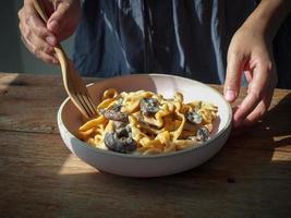 donna mano hold un' piatto di fatti in casa pasta con champignons fungo e carbonara salsa. foto