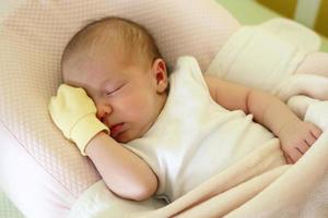 carino neonato bambino con giallo muffola su un' mano è addormentato su sua letto sotto beige lenzuolo. foto