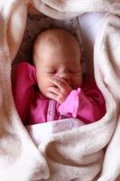 carino neonato bambino nel rosa baud è addormentato su sua letto sotto beige lenzuolo. foto