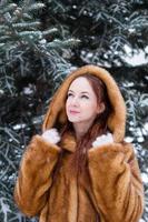 ritratto di giovane bellissimo donna con rosso capelli e blu occhi nel finto pelliccia cappotto su sfondo di inverno nevoso parco. foto
