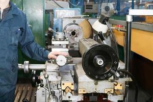 un' uomo Lavorando nel un' veste, tuta da lavoro sta Il prossimo per un industriale tornio per taglio, svolta coltelli a partire dal metalli, legna e altro materiali, girando, fabbricazione dettagli e scorta parti a il fabbrica foto