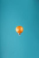arancia nel il modulo di un' leggero lampadina nel levitazione su un' blu sfondo. foto