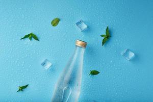 freddo acqua bottiglia, ghiaccio cubi, gocce e menta le foglie su un' blu sfondo. foto