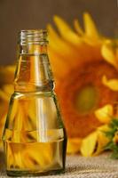 girasole olio nel un' bicchiere bottiglia e fiori su un' di legno sfondo, avvicinamento. foto