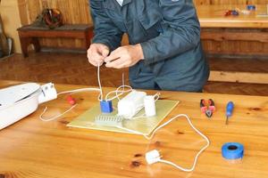 un' uomo Lavorando elettricista lavori, raccoglie il elettrico circuito di un' grande bianca strada lampada con fili, un' relè a un industriale pianta fabbrica foto