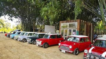 nakhon no, Tailandia - dicembre 5, 2020 molti austin mini bottaio o classico auto parcheggiata su strada con bambù foresta e Casa o casa sfondo con copia spazio. gruppo di Vintage ▾ o retrò veicolo. foto