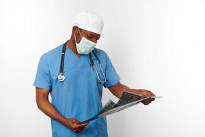 nero chirurgo medico uomo nel blu cappotto bianca berretto e chirurgo maschera detiene X raggio Immagine, bianca sfondo foto