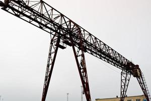 industriale ferro grande metallo cavalletto gru con un' gancio montato su il supporti per sollevamento e trasporto pesante carico, in movimento lungo il rotaie a il fabbrica. il gru è di ponte genere foto