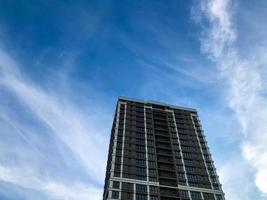 un' alto, multipiano bicchiere edificio nel un' bianca e Marrone città. il Casa ha balconi, elegante decorazione. ergonomico disposizione. contro il fondale di un' soleggiato blu soleggiato cielo foto