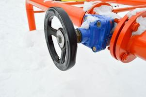 industriale spegnimento regolazione protettivo tubo raccordi. nero valvola per apertura, chiusura su un ferro arancia metallo tubo con flange, borchie, noccioline contro il sfondo di bianca neve nel inverno foto