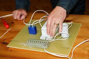 un' uomo Lavorando elettricista lavori, raccoglie il elettrico circuito di un' grande bianca strada lampada con fili, un' relè a un industriale pianta fabbrica foto