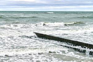 vista del mare blu con onde spumeggianti e frangiflutti in legno foto