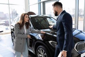 giovane donna acquirente discutere nel auto concessionaria con consulente, il concetto di acquisto un' auto su contratto di locazione foto