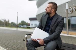 ritratto di riuscito maturo uomo d'affari con il computer portatile seduta Il prossimo per ufficio edificio foto