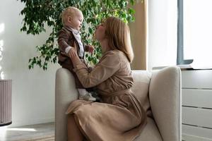 contento madre con sua poco bambino siamo seduta nel un' sedia foto