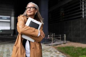 contento anziano uomo d'affari con un' il computer portatile nel il suo mani vicino il attività commerciale centro foto