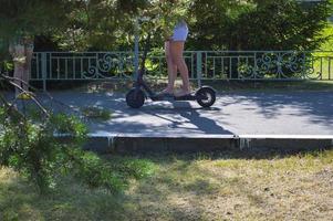 un' ragazza cavalcate un' a due ruote nuovo elettrico moderno scooter in piedi con Due piedi su un elettrico scooter su il strada nel il parco contro il fondale di alberi e natura foto