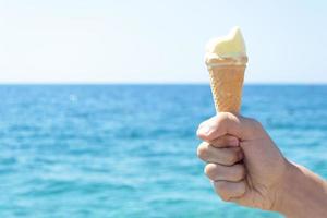 bambino mano Tenere ghiaccio crema di fronte blu mare foto