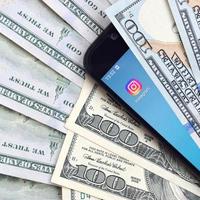 Kharkiv, Ucraina - Maggio 2, 2021 smartphone schermo con instagram App e lotto di centinaio dollaro fatture. attività commerciale e sociale networking concetto foto