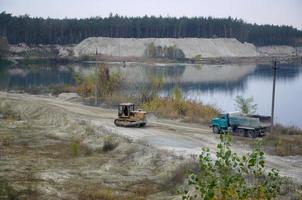 bruco caricatore e cumulo di rifiuti camion lavori a il a cielo aperto estrazione cava. pesante macchinari nel il Aperto fossa a fiume. dozer e camion su scavando operazioni foto