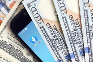 Kharkiv, Ucraina - Maggio 2, 2021 smartphone schermo con Facebook App e lotto di centinaio dollaro fatture. attività commerciale e sociale networking concetto foto