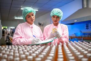 asiatico donna lavoratore con appunti è controllo Prodotto bottiglie di frutta succo su il produzione linea nel il bevanda fabbrica. fabbricante controlli qualità di cibo industria. foto