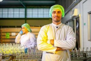 asiatico lavoratori con appunti è controllo Prodotto bottiglie di frutta succo su il produzione linea nel il bevanda fabbrica. fabbricante controlli qualità di cibo industria. foto