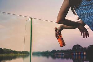 scollegato vita concetto. donna rilassante di natura nel campagna. potabile birra a il ponte di sul fiume nel estate foto