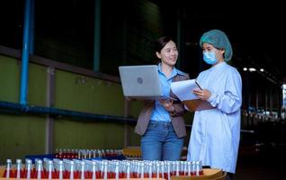 lavoratore di scienza nel bottiglia bevanda fabbrica indossare sicurezza cappello in posa mostrare opera per dai un'occhiata qualità di basilico seme produrre su trasportatore cintura prima distribuzione per mercato attività commerciale. foto