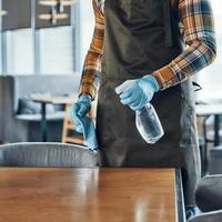 vicino su di uomo nel protettivo guanti pulizia tavolo per clienti mentre preparazione ristorante per Aperto durante pandemia foto