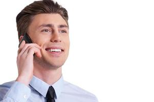 bene parlare. bello giovane uomo nel vestito formale parlando su il mobile Telefono e sorridente mentre isolato su bianca foto