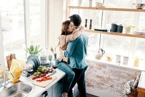 amore è nel il aria. bellissimo giovane coppia Abbracciare una persona mentre in piedi nel il cucina a casa foto