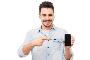 copia spazio su il suo telefono. allegro giovane uomo mostrando mobile Telefono e sorridente mentre in piedi contro bianca sfondo foto