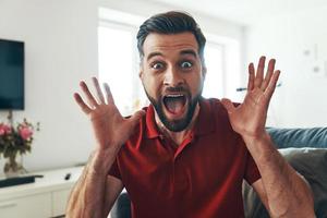 bello giovane uomo nel casuale capi di abbigliamento guardare a telecamera e fabbricazione un' viso mentre la spesa tempo in casa foto