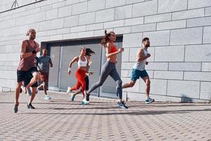 pieno lunghezza di giovane persone nel gli sport capi di abbigliamento jogging mentre esercizio su il marciapiede all'aperto foto