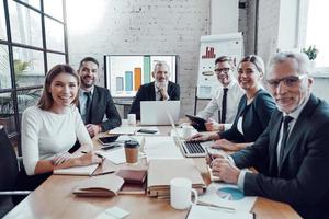 riuscito attività commerciale squadra sorridente e guardare nel il telecamera mentre Lavorando nel il moderno ufficio foto