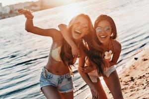 così tanto divertimento insieme. Due attraente giovane donne nel costumi da bagno sorridente mentre la spesa spensierato tempo su il spiaggia foto