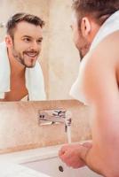 mattina routine. bello giovane uomo lavaggio mani nel bagno mentre in piedi nel davanti di il specchio foto