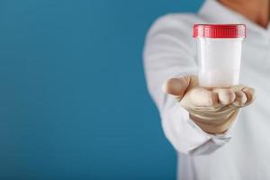 un' medico guantato mano Tenere un' bottiglia di un' contenitore con un' sperma campione per medico analisi. foto