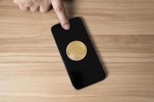 dito toccante il smartphone e bitcoin su di legno tavolo concetto criptovaluta scambio. tecnologia e investimento digitale. finanza, commerciante, investitore, oro bitcoin denaro contante foto