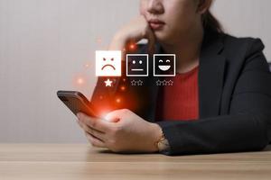 attività commerciale donne Selezionare cattivo viso emoticon su virtuale toccare schermo a smartphone. cattivo revisione, cattivo servizio antipatia cattivo qualità, Basso valutazione, sociale media non bene foto