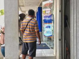 blitar, Indonesia - ottobre 20 2022 un' casualmente vestito uomo in piedi nel linea a un' banca rakyat Indonesia ATM nel il pomeriggio nel blitar foto