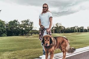 grande compagno. pieno lunghezza di bello giovane uomo in piedi con il suo cane mentre la spesa tempo all'aperto foto