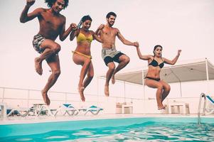 godendo piscina festa. gruppo di bellissimo giovane persone guardare contento mentre salto in il nuoto piscina insieme foto